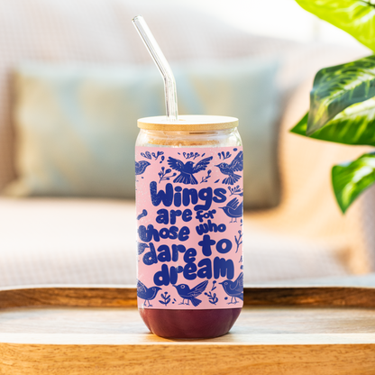  16oz reusable glass sipper with bamboo lid and straw, featuring the phrase 'Wings Are for Those Who Dare to Dream' in bold blue lettering with bird illustrations on a pink background. Displayed on a kitchen counter, perfect for adding charm to your daily hydration routine