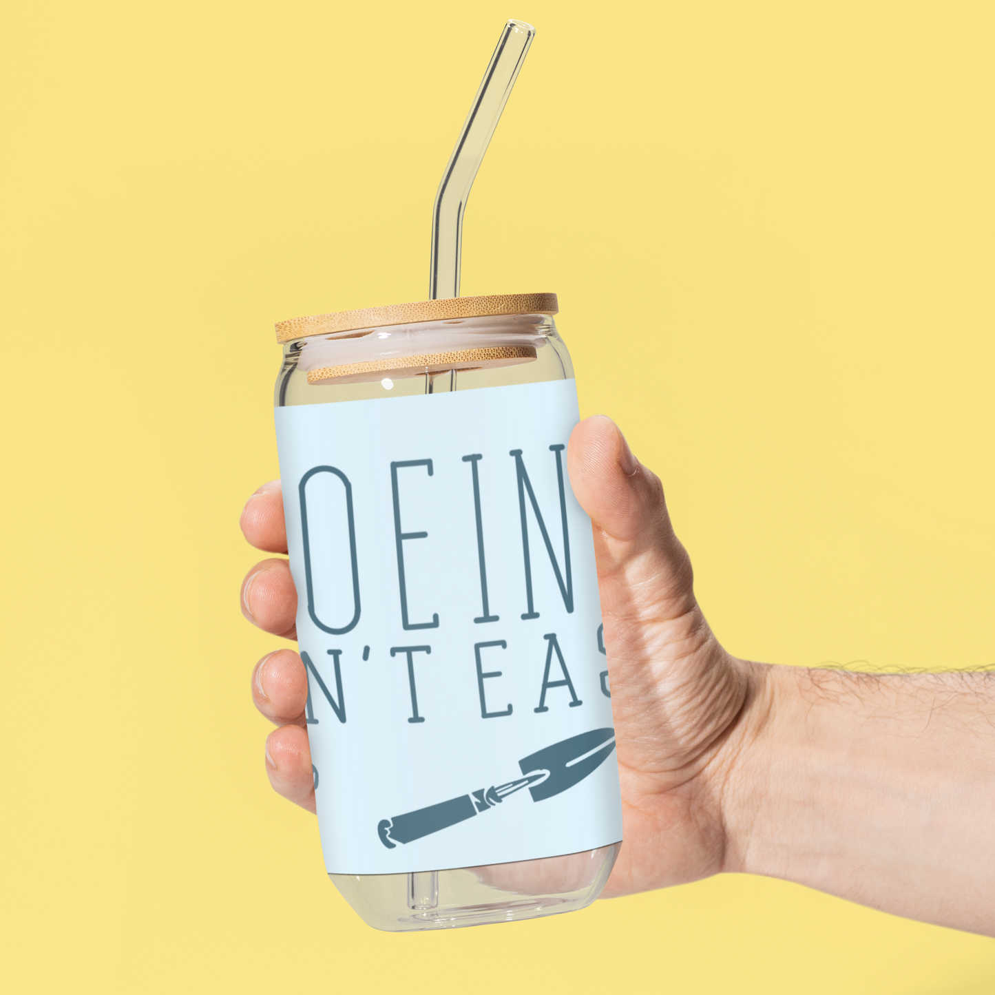 Reusable glass tumbler featuring the phrase 'Hoeing Ain't Easy' with garden tool illustrations, displayed against a bright yellow background. Includes a bamboo lid and clear straw.