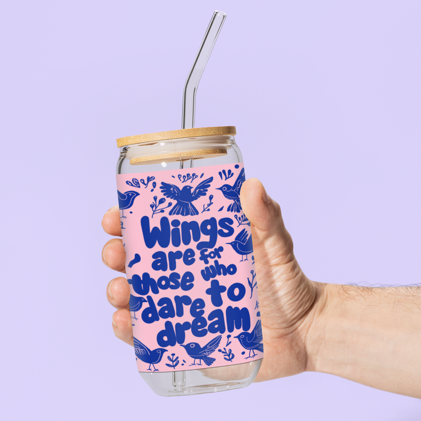 16oz reusable glass sipper with bamboo lid and straw, held by a hand against a pastel purple background. Features the inspirational phrase 'Wings Are for Those Who Dare to Dream' in bold blue text with bird illustrations on a pink background.